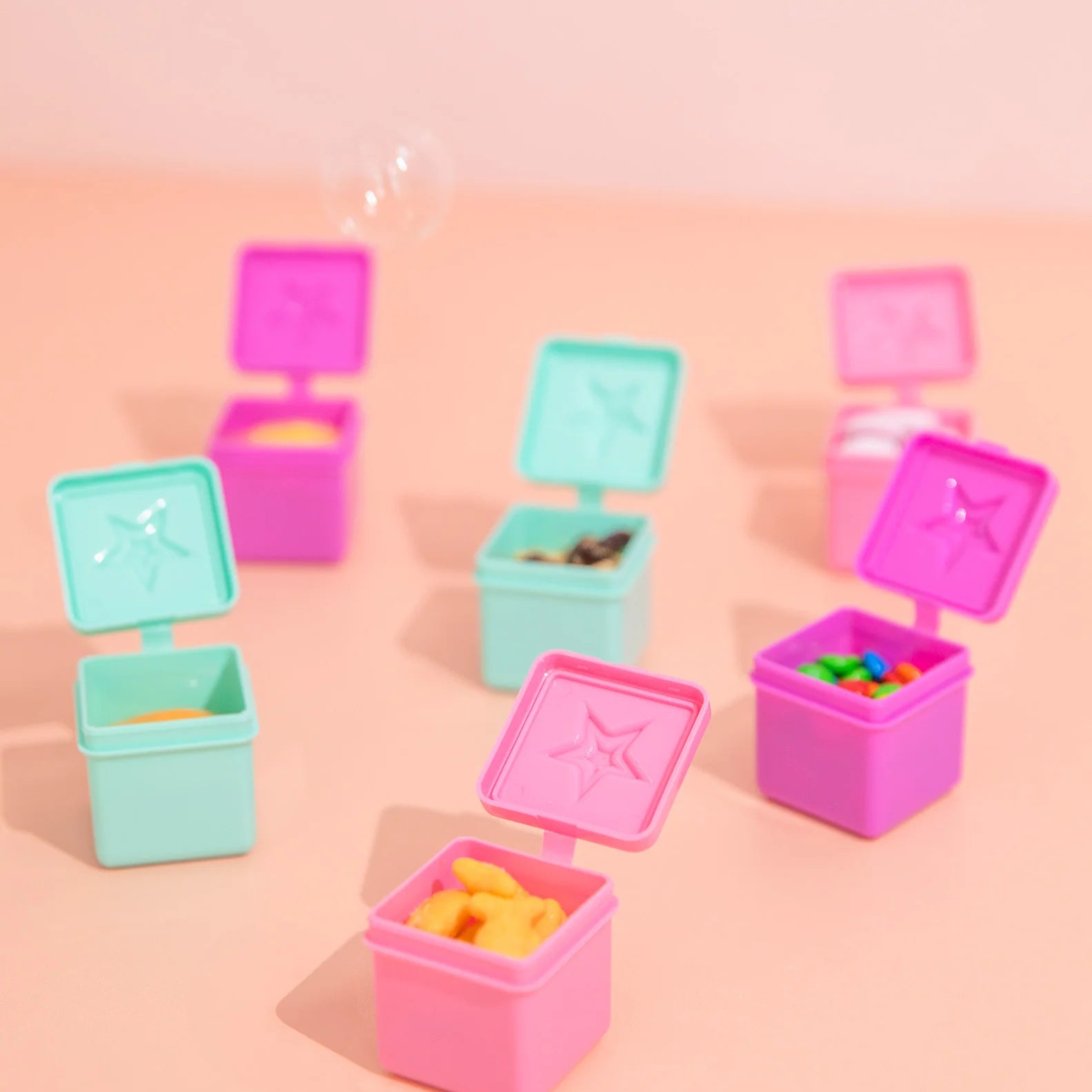 Set of small colorful plastic containers with lids on a pink background
