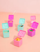 Set of small colorful plastic containers with lids on a pink background