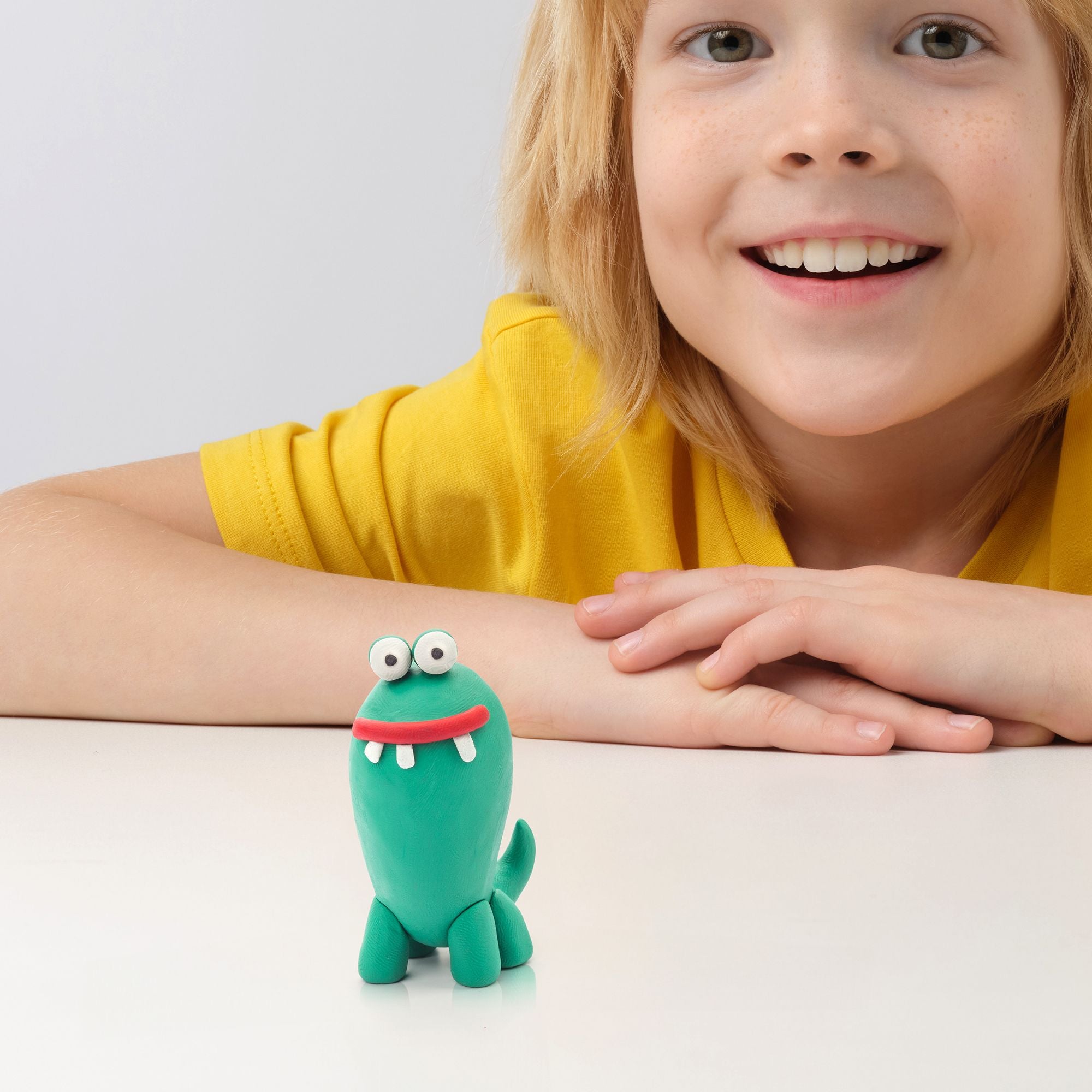 Child wearing a yellow shirt with a green toy dinosaur on a light background from hey clay monster set