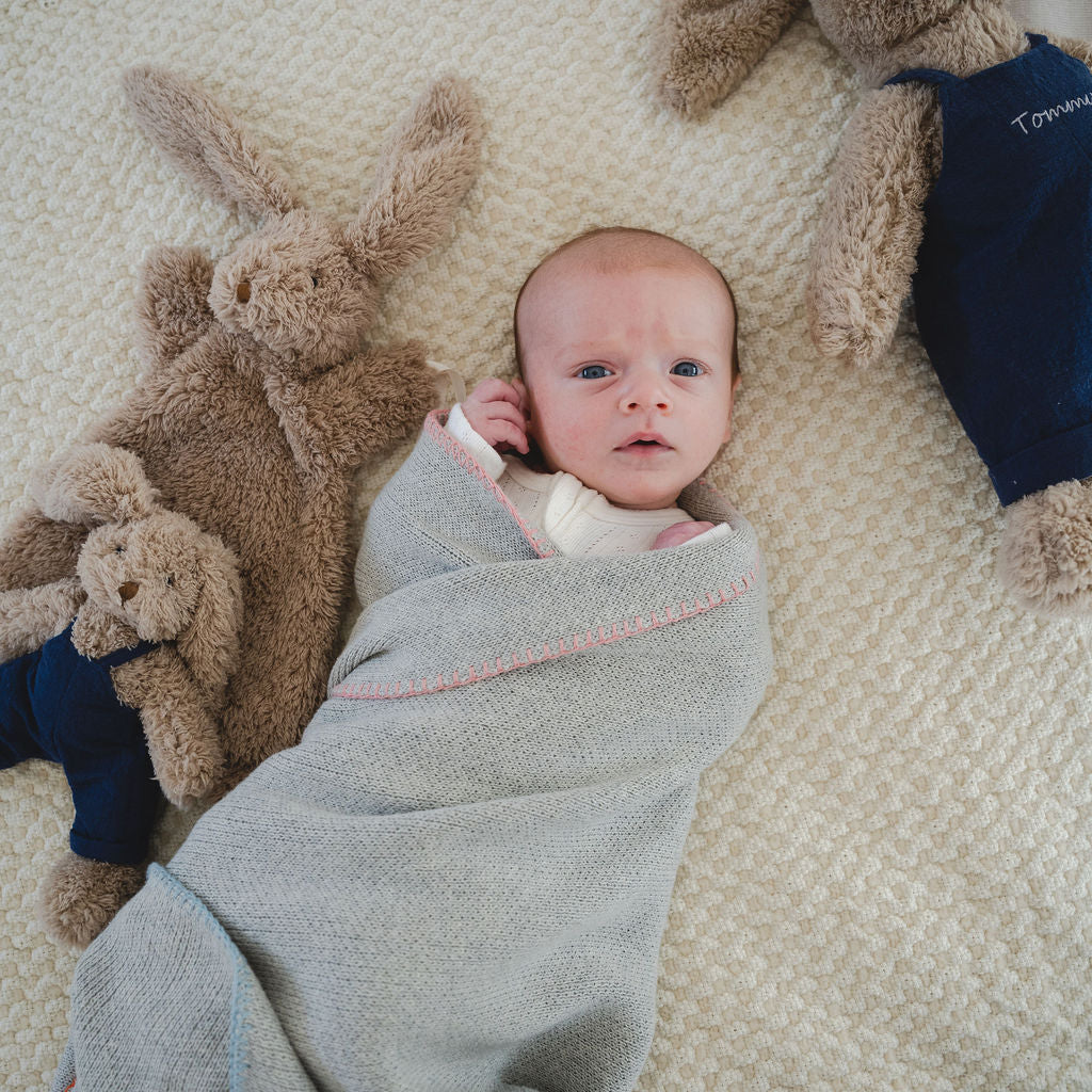 Newborn baby wrapped in a gray blanket with teddy bears on a textured surface